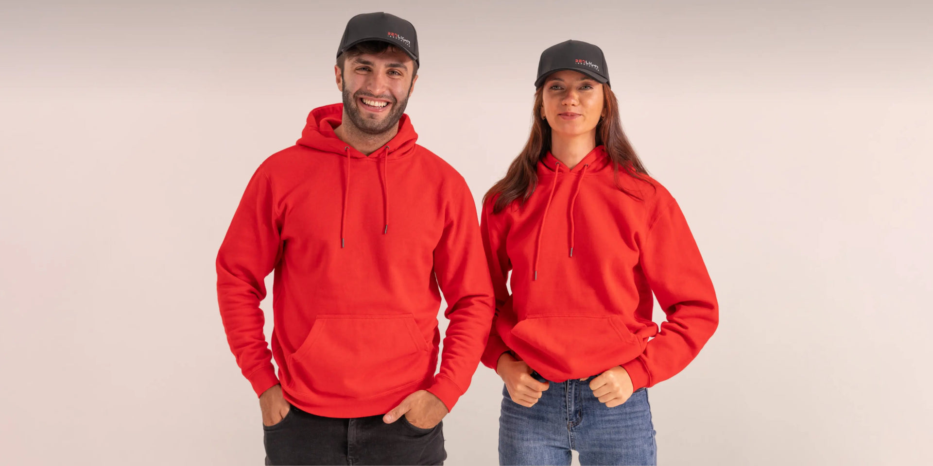 A man and a woman wearing RedLight Innovation red light hats, in red hoodies against a grey studio background