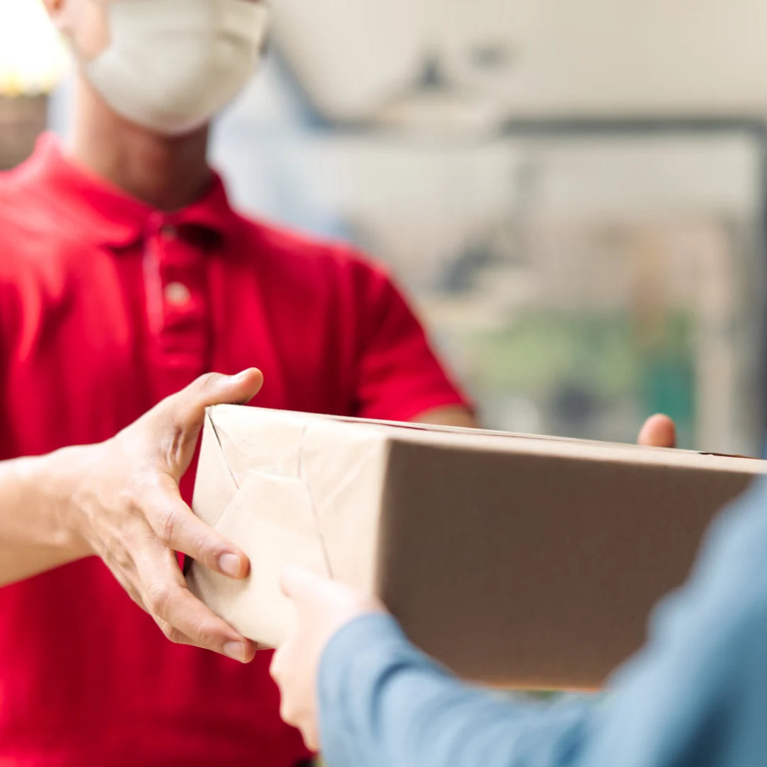 Person in red shirt and face mask handing over a package to another person.